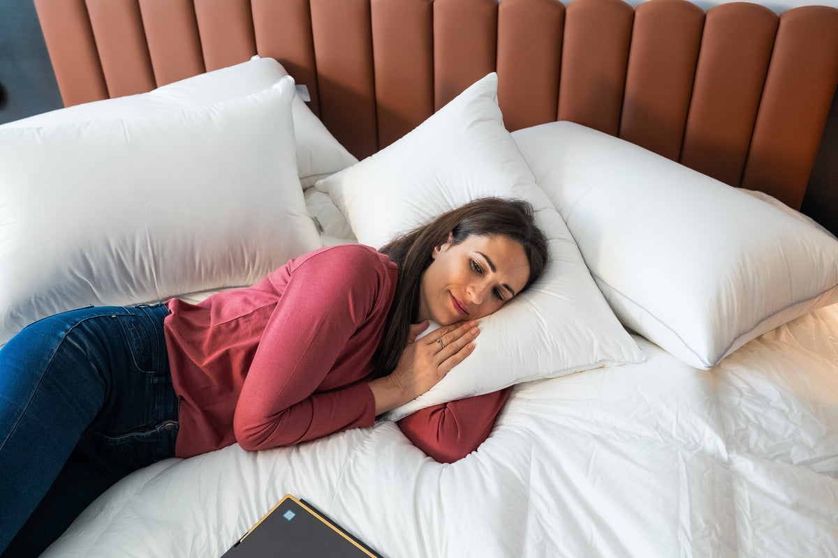 Woman resting on a plush white down pillow in a bed with a tan channel-tufted headboard