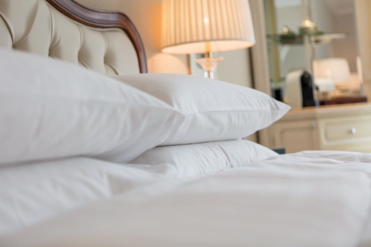 White pillows and crisp white bedding on a made bed beside a lit lamp in a warm hotel room