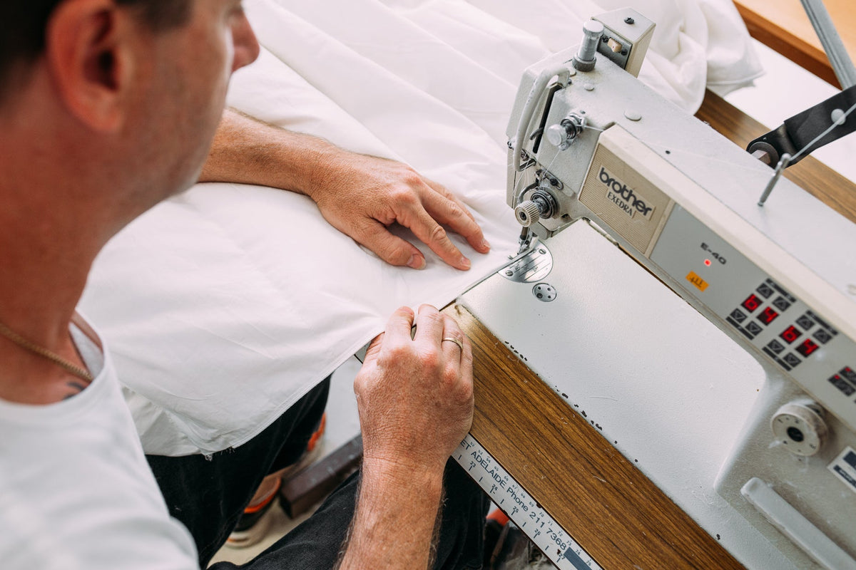 Maker guiding white quilt fabric through an industrial Brother sewing machine in an Australian workshop