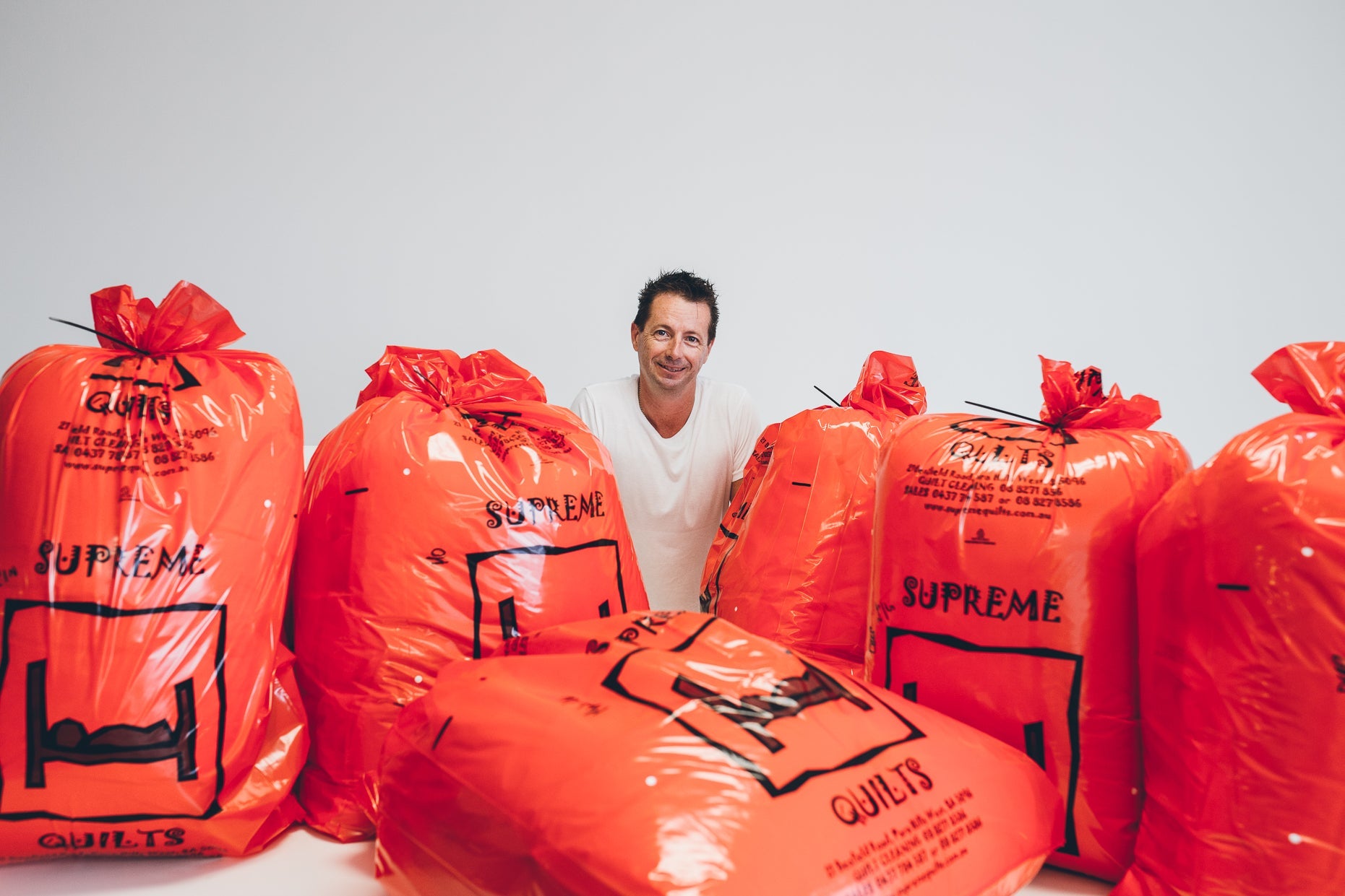 Owner of Supreme Quilts Australia Standing in behind packaged products in Supreme Quilts’ red and black eco friendly packaging. The items are European Duck and Goose Down Quilts, Duvets, Blankets, Pillows, and Mattress Toppers Made in Australia

